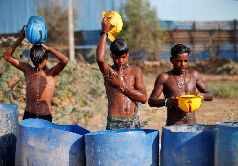 Workers use their helmets to pour water to cool off near a construction site on a hot summer day on the outskirts of Ahmedabad