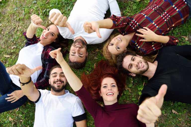 friends-with-thumbs-up-lying-lawn-park
