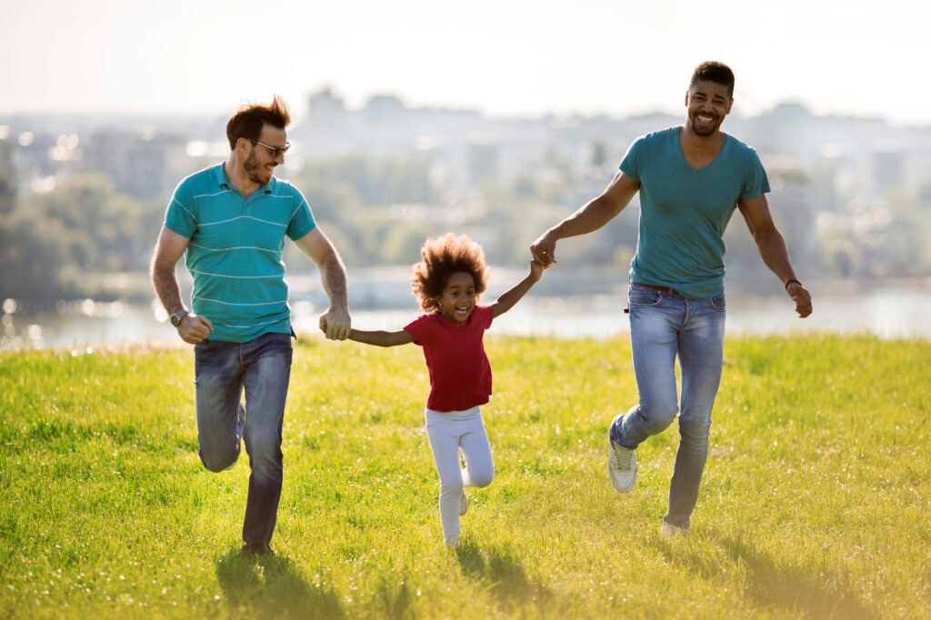 Two happy men running with African American little girl outdoors.